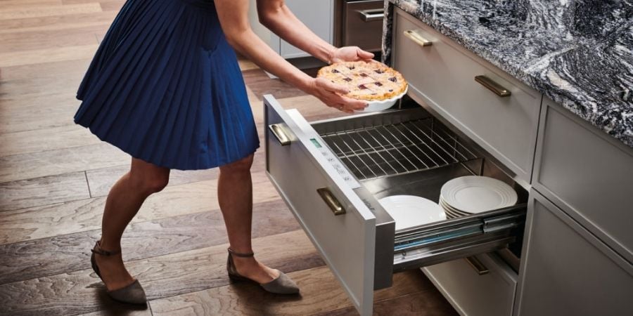 woman in blue dress putting pie in warming drawer